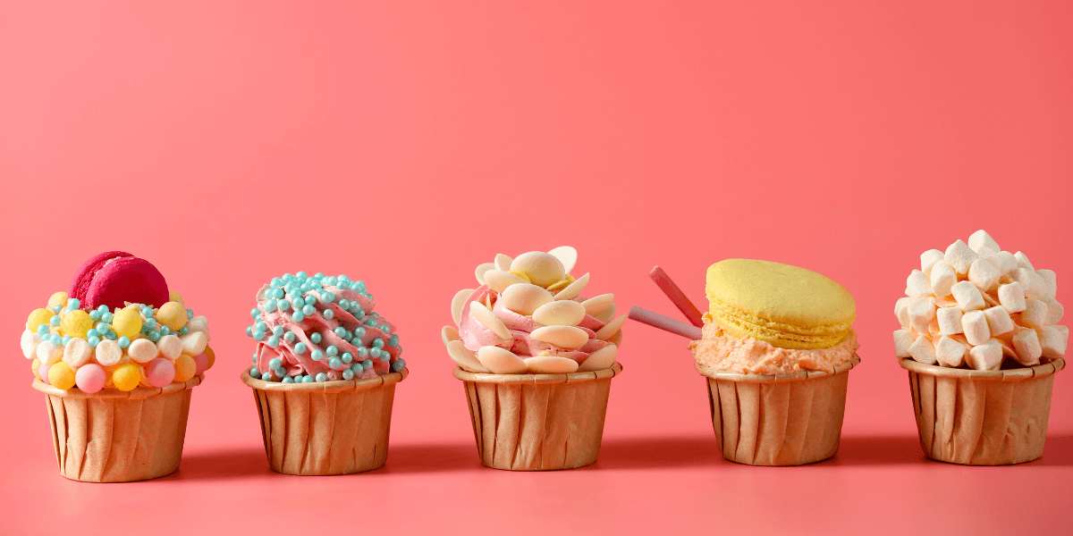 A row of different, beautifully decorated cupcakes with a pink background